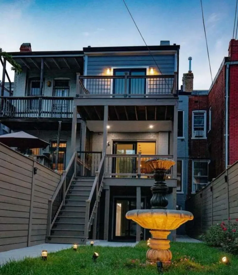 Rear of a house at dusk with stacked decks, a lit fountain, and path lights.