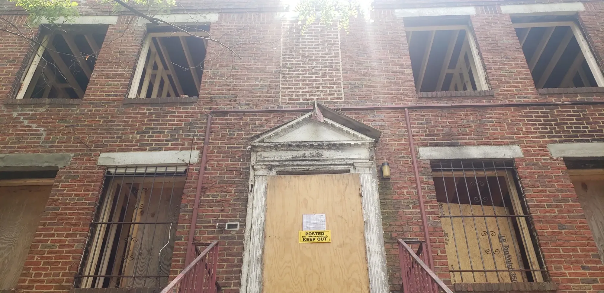 Brick building front secured with plywood, window bars, and a posted notice.