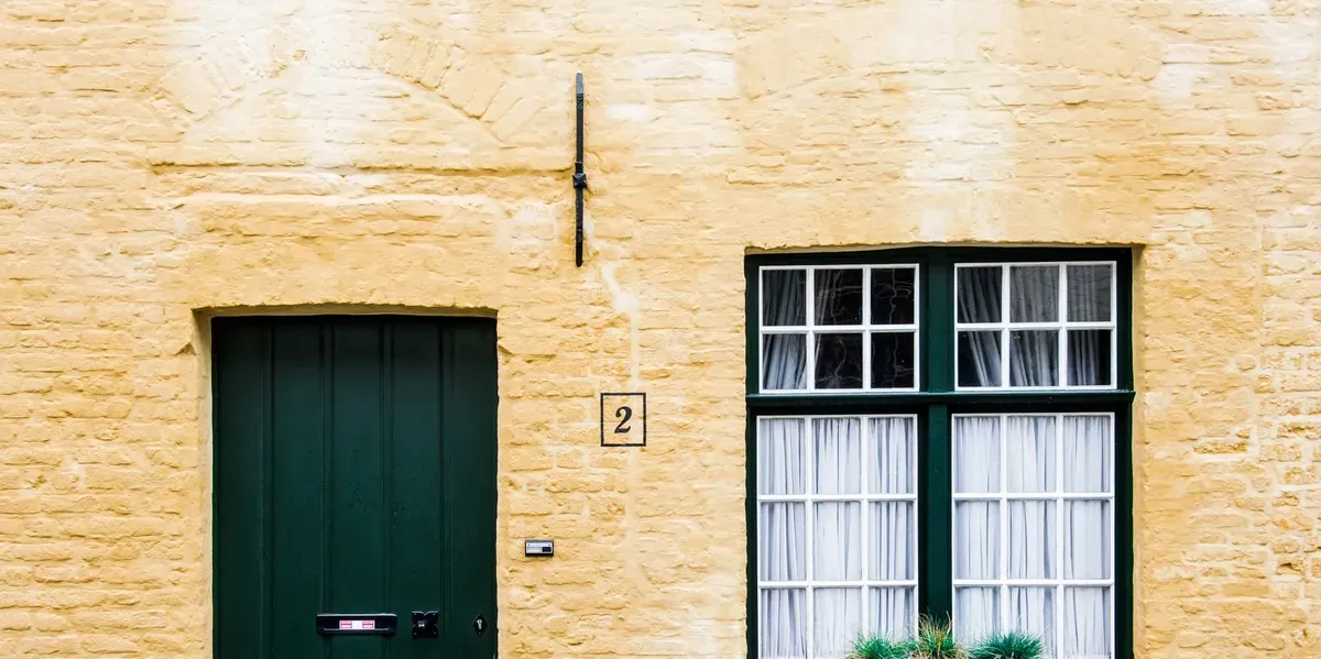 Yellow masonry facade with a dark green door and a large window.