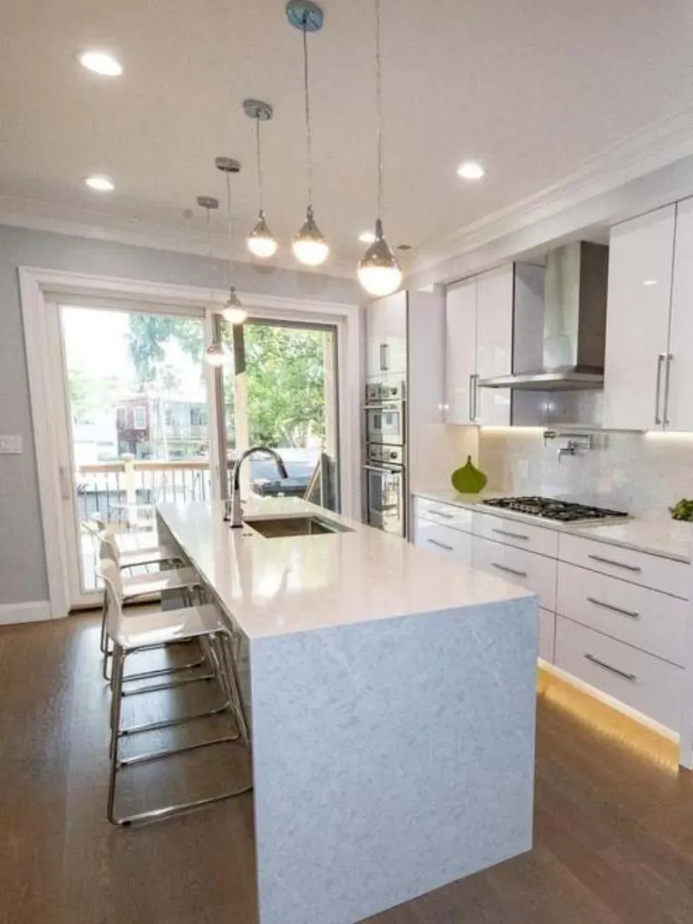 White kitchen island with pendant lights and a sliding door to a deck.