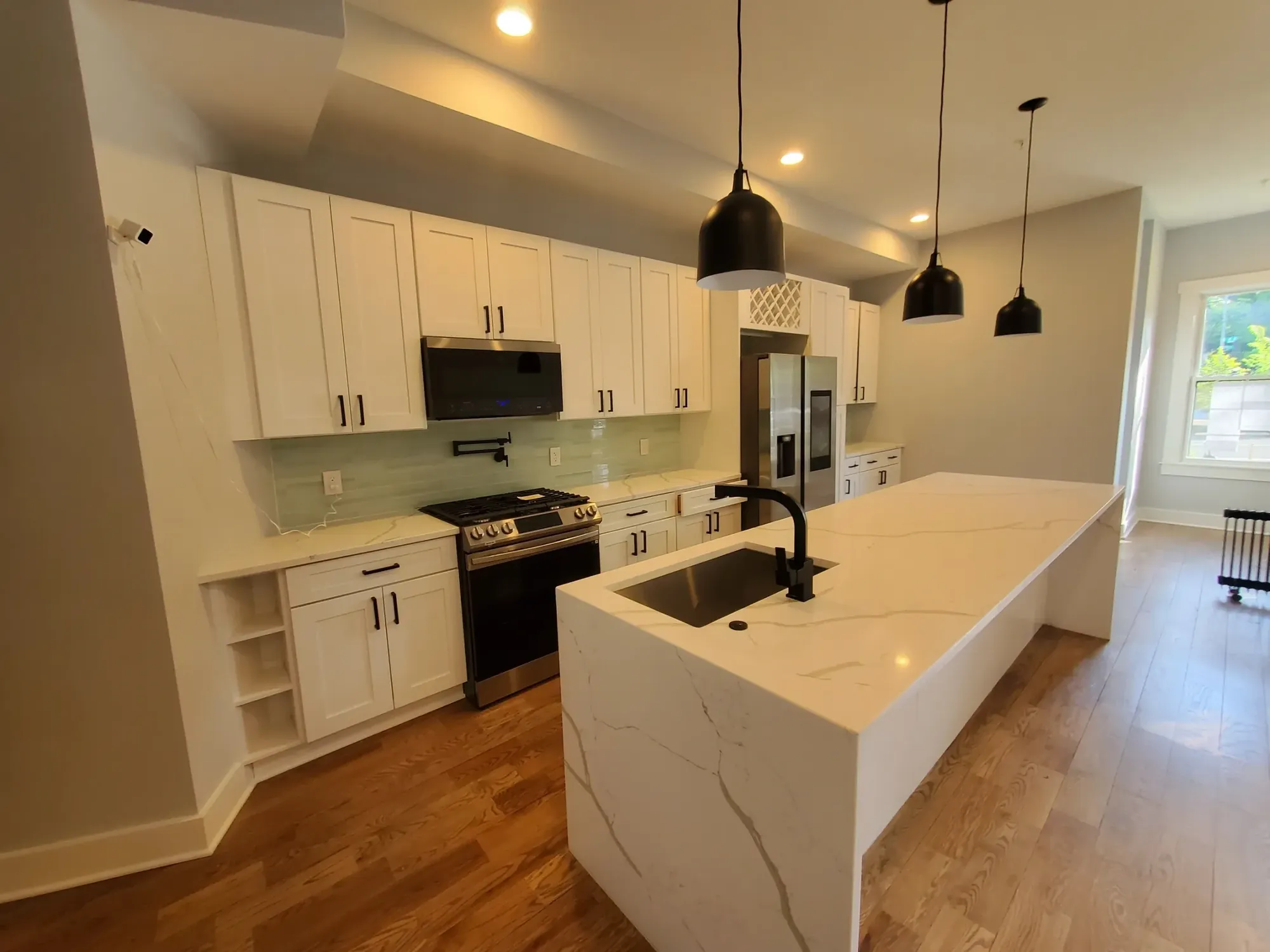 White kitchen with a marble island, black pendants, and wood floors.